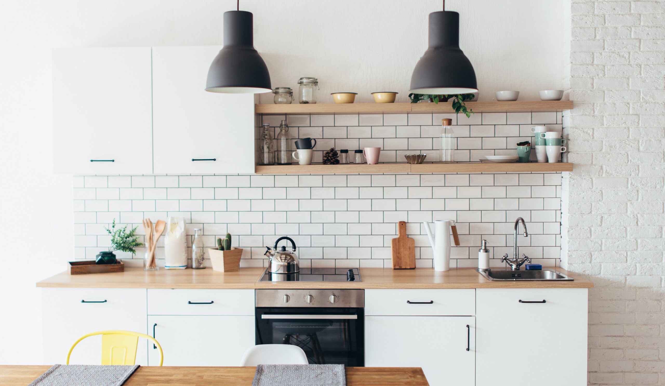 Comment rendre une cuisine plus lumineuse avec des murs blancs, une crédence en carrelage brillant et des étagères en bois clair.
