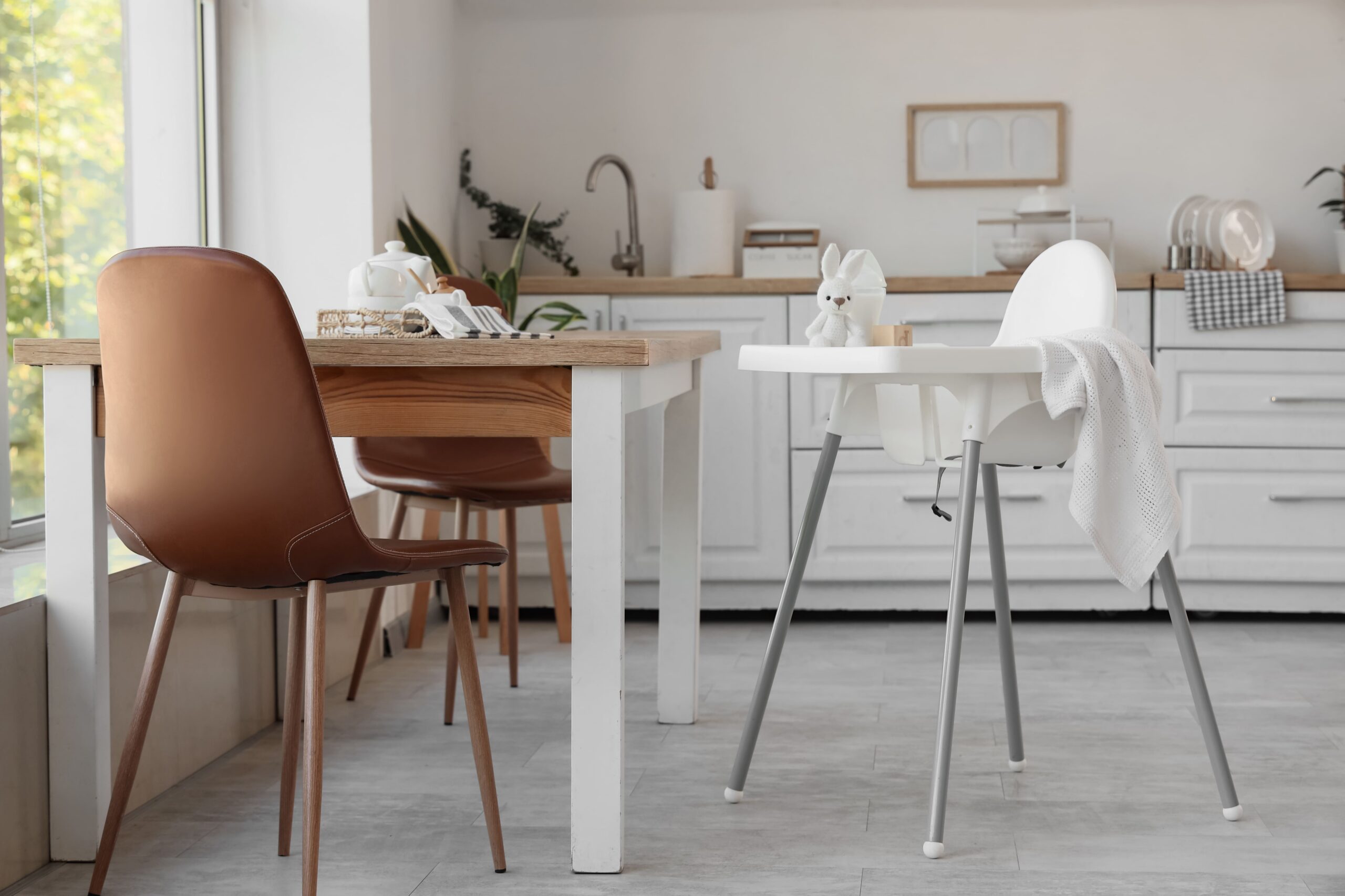 Coin repas aménagé dans une petite cuisine blanche moderne avec table en bois et chaise haute pour bébé.
